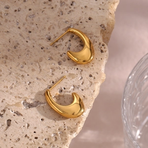 Close-up of golden crescent hoop earrings with a polished finish on a natural rock base