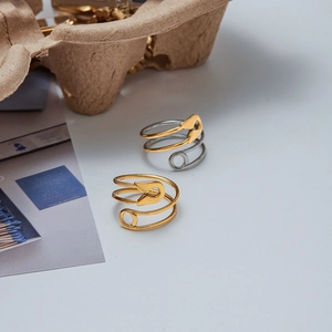 Dettaglio di anelli a spilla da balia multistrato in oro e argento su un display minimalista