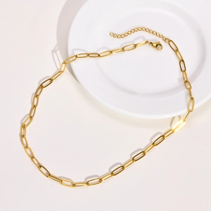 Detail of a golden paperclip chain necklace with a lobster clasp on a ceramic plate