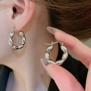 Detailed close-up of C-shaped silver metallic earrings with elegant twisted bead texture
