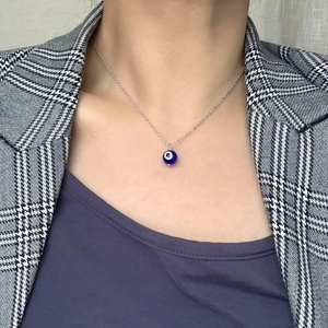 Collier pendentif œil bleu turc sur chaîne argentée porté avec un blazer pied-de-poule