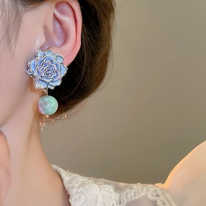 Close-up of blue rose earrings with gold edges and gradient green and pink bead pendant