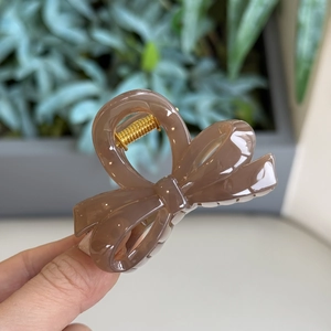 Detailed view of coffee brown bow-shaped hair claw clip with gold metal spring mechanism