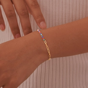 Detail of gold paperclip chain bracelet featuring vibrant square cut rainbow gemstones