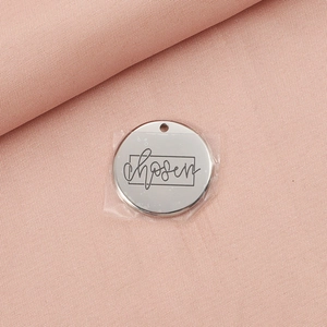 Detail of silver stainless steel round pendant with engraved chosen text on pink fabric