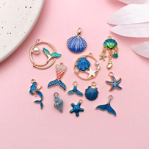 Set of 13 gold mermaid and starfish charms with blue enamel and pearls on pink background