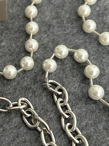 Detail of white pearls stitched with a silver oval link chain on a gray felt background