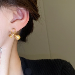 Macro side view of crossed gold ball stud earrings featuring a minimalist twisted design