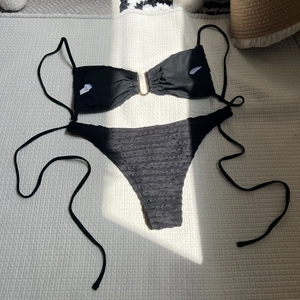 Detailed view of black textured fabric bikini with metallic ring and side tie strings