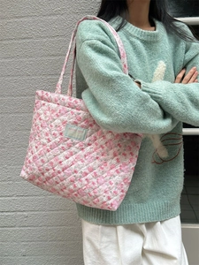 Quilted pink floral tote bag worn over the shoulder against a brick wall background