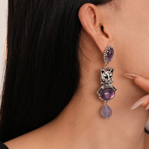 Close-up of vintage silver earrings featuring purple resin gems and a small cat design