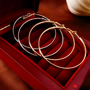 Détail de grandes boucles d'oreilles créoles dorées et argentées sur velours rouge
