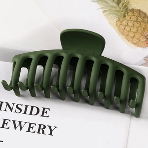 Detail of a large matte dark green hair claw clip with multiple teeth on a magazine