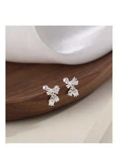 Macro shot of silver bowknot bell stud earrings with secure screw back on wood
