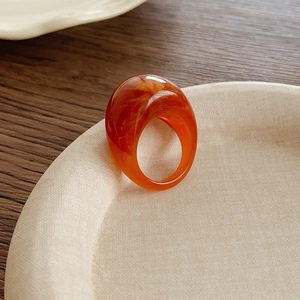 Gros plan d'une bague bombée en résine ambrée avec texture marbrée sur un plateau
