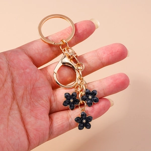 Detail of a gold keychain featuring three elegant black flower pendants held in hand
