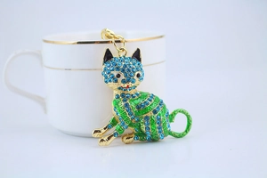 Detail of a golden cat keychain with blue rhinestones and green enamel on a white surface