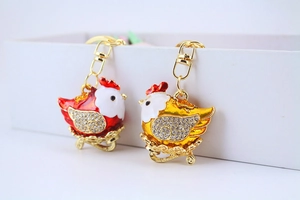 Close-up of red and gold hen keychains with crystals in a white gift box