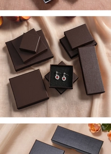 Detailed view of dark brown linen texture jewelry boxes with elegant earrings on silk fabric