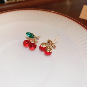 Macro shot of sweet red cherry stud earrings with green crystal leaves on a white ceramic plate