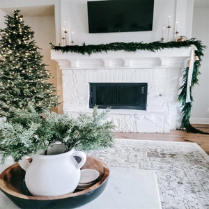 Close-up of realistic PE Norfolk pine garland decorating a white fireplace for Christmas