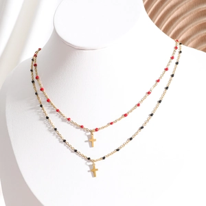 Detailed view of gold double-layer necklace with red and black beads and cross pendants
