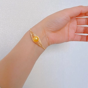 Bracciale rigido minimalista in filo dorato con una perla dorata tonda su sfondo bianco