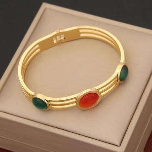 Gold hollow cuff bracelet with green cat eye stones and red gem on beige display