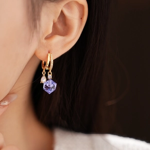 Close-up of a gold hoop earring with sparkling purple crystal and zircon on a model