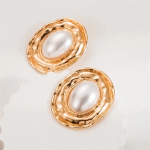 Detail of irregular leaf-shaped gold earrings with textured edges and white pearl core