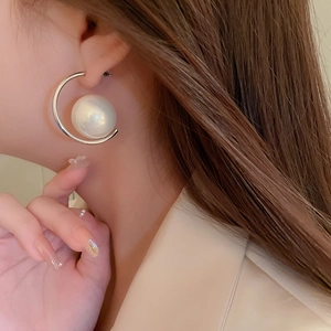 Detailed side view of a C-shaped silver earring with a large white pearl on model