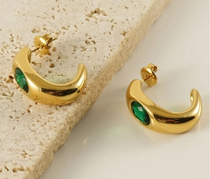 Close-up of gold C-shaped earrings with green emerald-style stones on a stone display