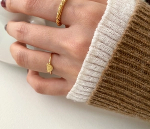 Golden bear shaped ring and twisted metal band worn by a model holding a white cup