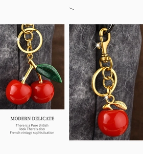Detailed close-up of red resin cherry keychain with golden hardware on grey fabric