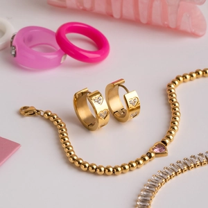 Détail de boucles d'oreilles cœur dorées et bracelet avec perle cœur en zircon rose