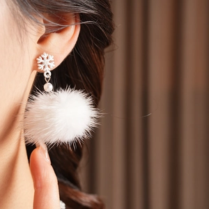 Detailed view of winter snowflake earrings with pearls and soft white pom-poms on model