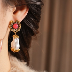 Detailed close-up of a vintage gold flower earring with red gemstone and baroque pearl