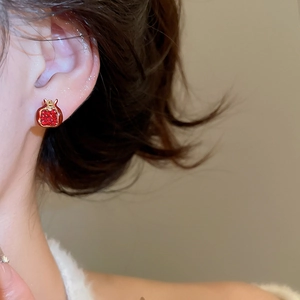Close-up of pomegranate-shaped gold earrings with red stones on a model's ear