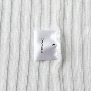 Detail shot of the 100% viscose ribbed fabric and size label on the white knit dress