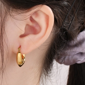Close-up of a polished gold-plated hollow U-shaped earring on a model ear lobe