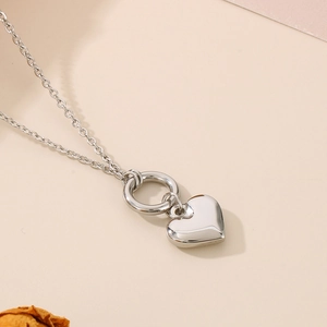Detail of silver heart pendant necklace with a circle ring clasp on beige background