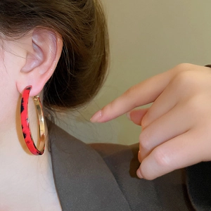 Close-up of model wearing large gold-edged leopard print hoop earrings in red and black