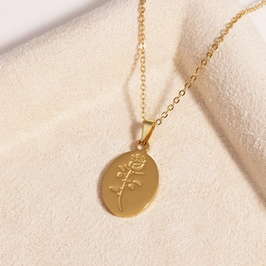Detail of a gold titanium steel necklace with a rose engraved oval pendant on beige fabric