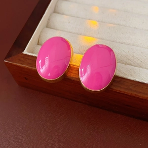 Detail of pink oval enamel stud earrings in gold base on a brown wooden jewelry box
