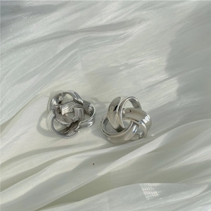 Detailed macro view of silver twisted earrings on white silk with mirror polish finish