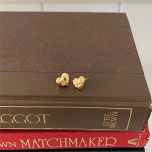 Close-up of heart-shaped gold stud earrings with bow texture on vintage books