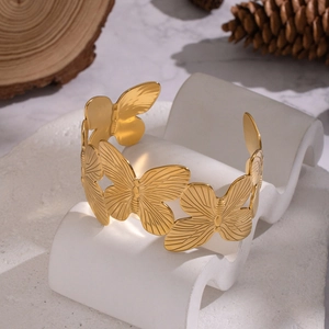 Detail shot of golden butterfly open cuff bracelet with intricate hollowed wings on a stand