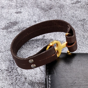Detailed close-up of dark brown leather bracelet with golden anchor buckle and silver rivets