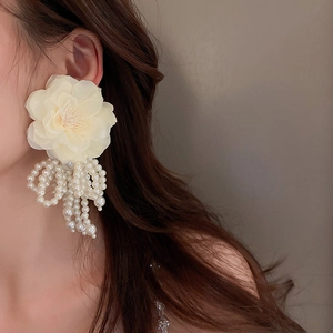 Close-up of model wearing large cream flower earrings with white pearl tassels