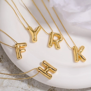 Chic gold balloon initial pendant necklaces displayed on a minimal white ceramic plate